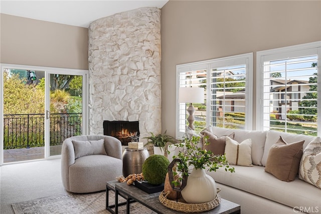 carpeted living room featuring a stone fireplace, a high ceiling, and a wealth of natural light