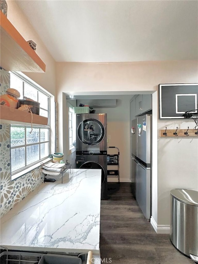 kitchen featuring gray cabinets, stainless steel refrigerator, stacked washer and clothes dryer, light stone counters, and dark hardwood / wood-style flooring