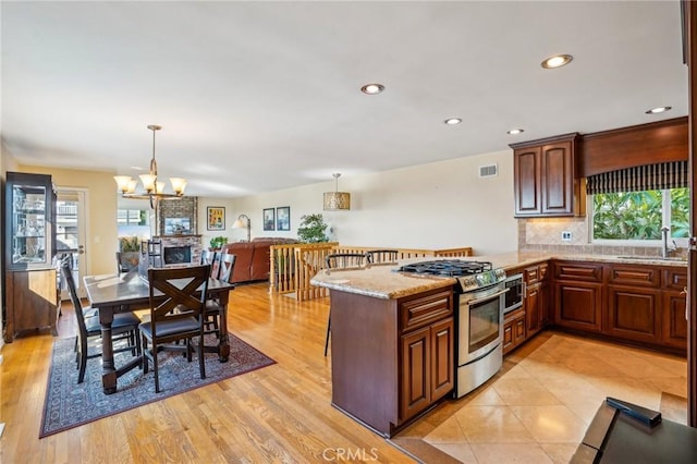 kitchen with sink, gas stove, hanging light fixtures, light wood-type flooring, and backsplash