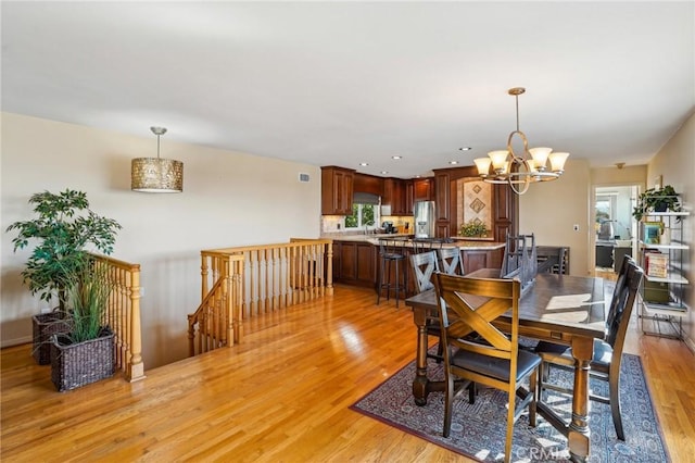 dining room with a notable chandelier, sink, and light wood-type flooring