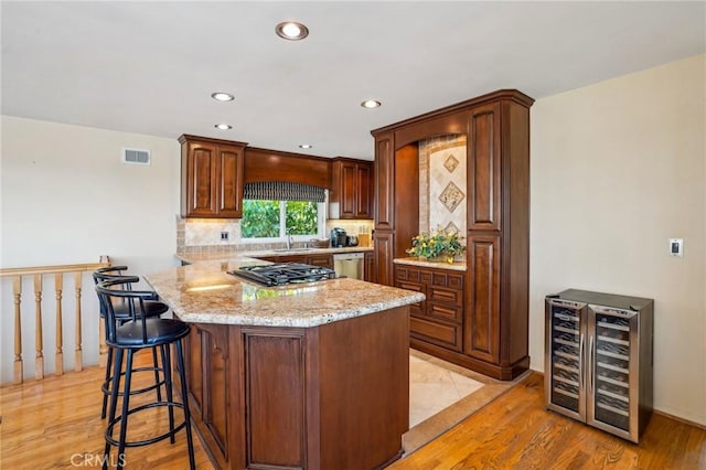 kitchen with appliances with stainless steel finishes, sink, wine cooler, decorative backsplash, and light stone counters