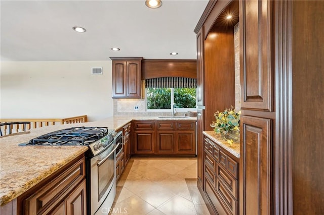 kitchen featuring a kitchen bar, sink, stainless steel gas stove, tasteful backsplash, and kitchen peninsula