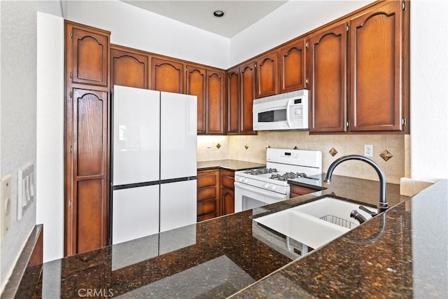 kitchen with tasteful backsplash, white appliances, sink, and dark stone countertops