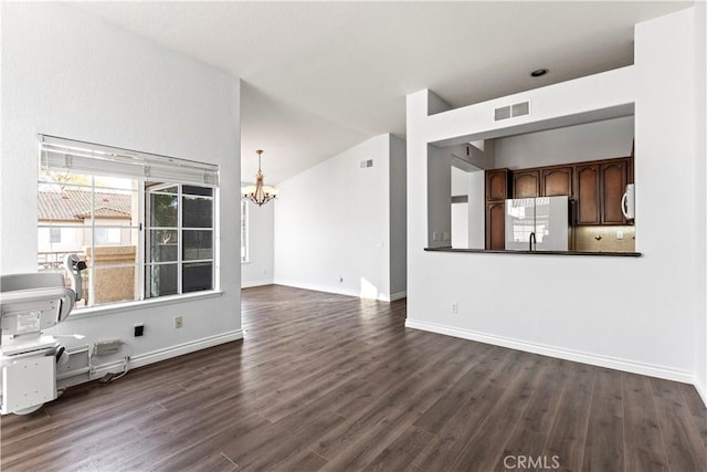 unfurnished living room featuring dark wood-type flooring, vaulted ceiling, and a notable chandelier