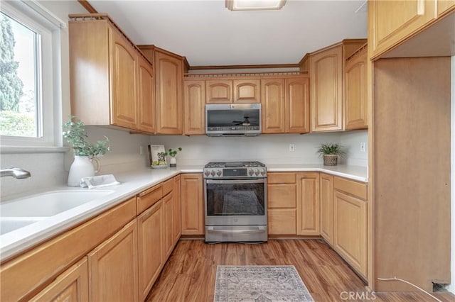 kitchen with appliances with stainless steel finishes, sink, light brown cabinetry, and light hardwood / wood-style flooring