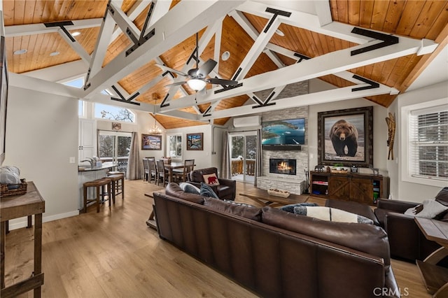 living room with a stone fireplace, lofted ceiling with beams, light hardwood / wood-style flooring, wooden ceiling, and ceiling fan