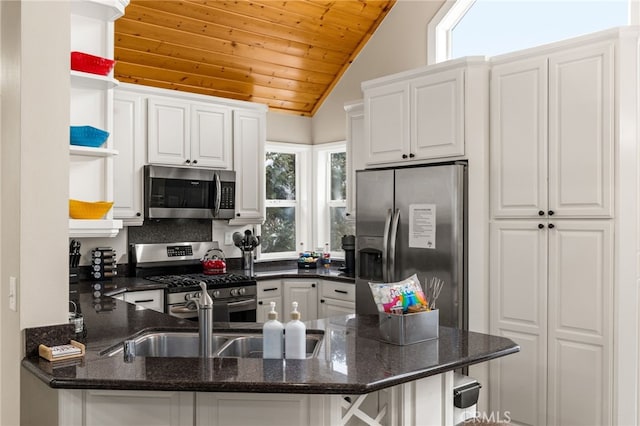 kitchen featuring white cabinetry, stainless steel appliances, kitchen peninsula, and dark stone counters