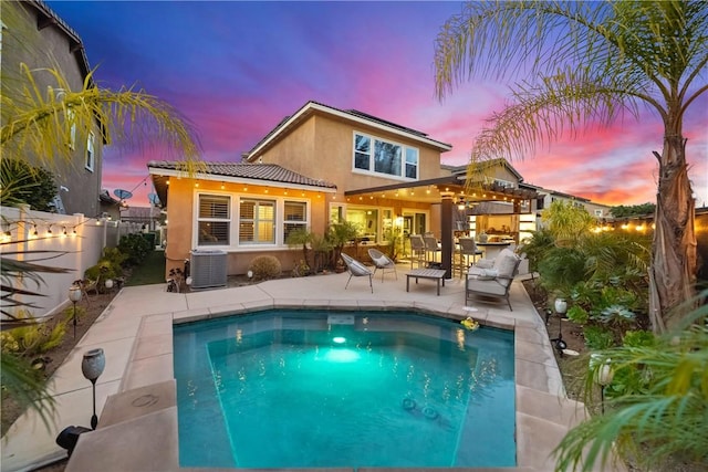 back of house at dusk with central AC unit, a fenced backyard, outdoor dry bar, stucco siding, and a patio area