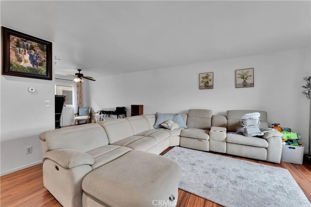 living area with light wood-style floors, baseboards, and ceiling fan