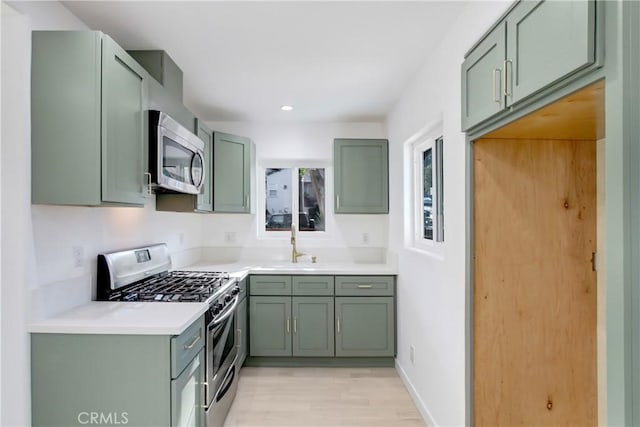 kitchen with stainless steel appliances, green cabinets, and light wood-type flooring