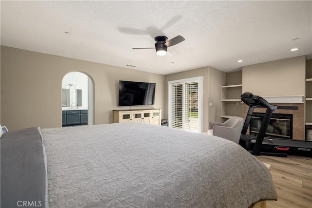 bedroom with a tile fireplace, connected bathroom, ceiling fan, and light hardwood / wood-style floors