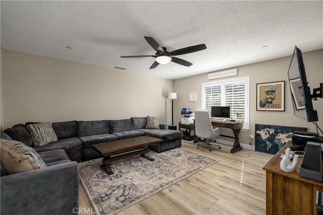 living room with ceiling fan, a textured ceiling, and light wood-type flooring