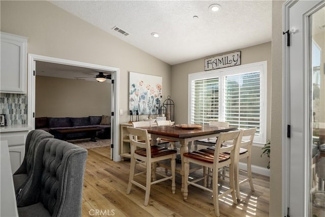 dining area featuring vaulted ceiling, ceiling fan, a textured ceiling, and light wood-type flooring