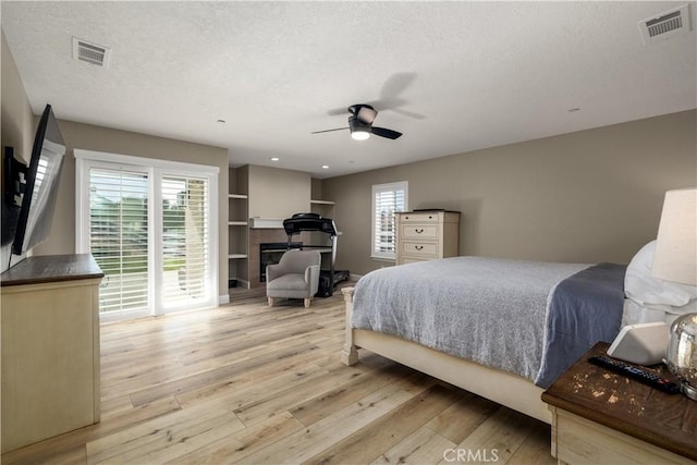 bedroom featuring multiple windows, a tile fireplace, a textured ceiling, and light wood-type flooring