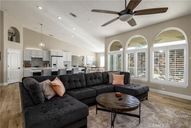 living room with high vaulted ceiling, sink, ceiling fan, a textured ceiling, and light hardwood / wood-style flooring