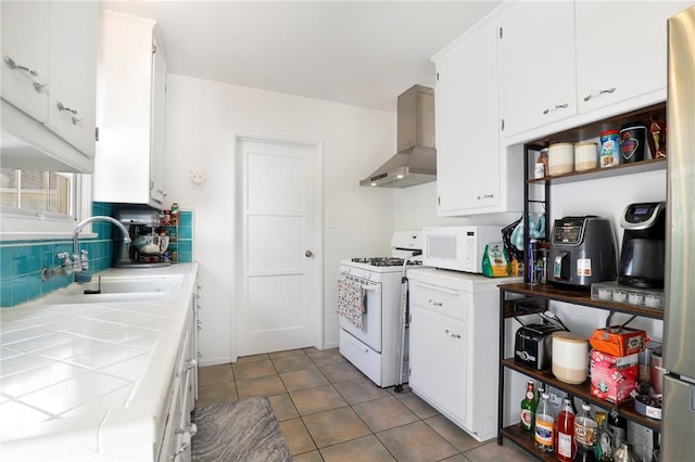 kitchen featuring sink, tile countertops, light tile patterned floors, white appliances, and wall chimney range hood