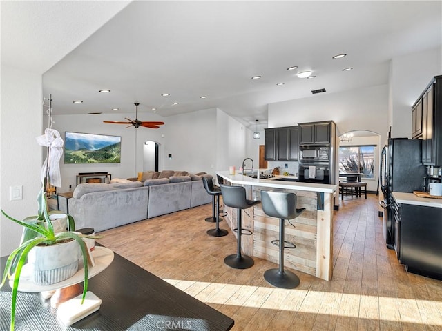 kitchen featuring sink, light wood-type flooring, a kitchen breakfast bar, ceiling fan, and black appliances