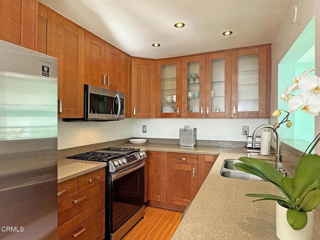 kitchen with light stone counters, stainless steel appliances, sink, and light wood-type flooring