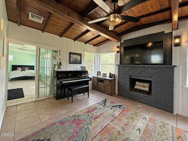 interior space featuring light tile patterned flooring, vaulted ceiling with beams, wood ceiling, a brick fireplace, and ceiling fan