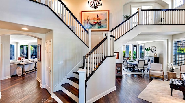 stairway with wood-type flooring, plenty of natural light, a towering ceiling, and a chandelier