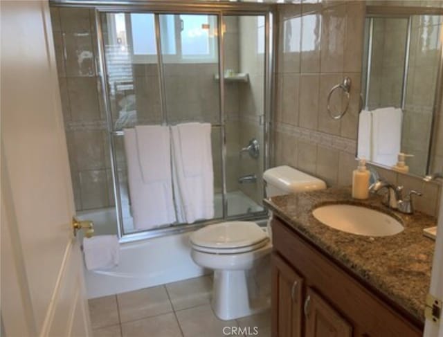 full bathroom featuring tile patterned floors, toilet, combined bath / shower with glass door, tile walls, and vanity