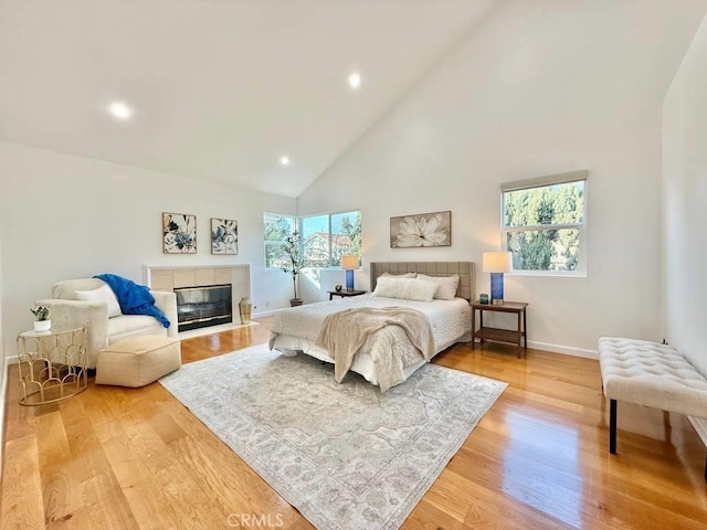 bedroom with a fireplace, light hardwood / wood-style flooring, and high vaulted ceiling