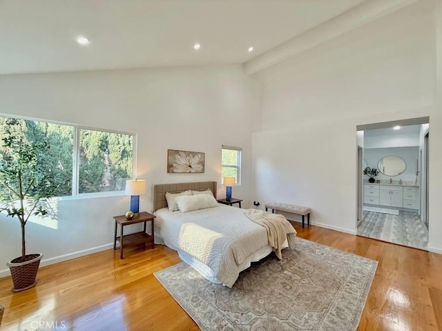 bedroom featuring connected bathroom, beam ceiling, light hardwood / wood-style flooring, and high vaulted ceiling