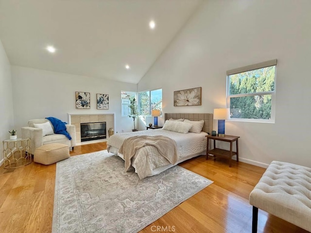 bedroom featuring high vaulted ceiling, a tiled fireplace, and light hardwood / wood-style floors