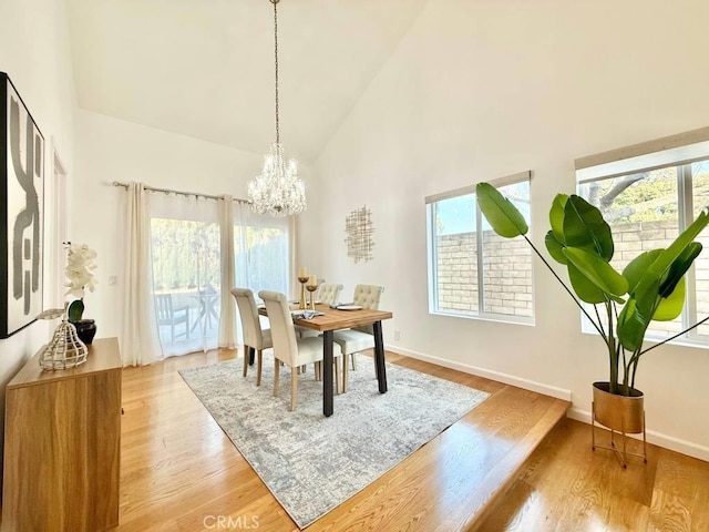 dining area with a chandelier, high vaulted ceiling, and light hardwood / wood-style flooring