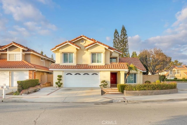 mediterranean / spanish-style home featuring a garage, concrete driveway, a tiled roof, and stucco siding