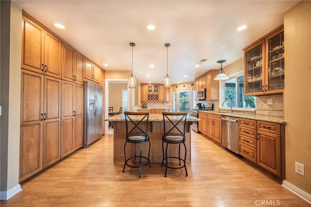 kitchen featuring sink, stainless steel appliances, a center island, light stone countertops, and decorative backsplash