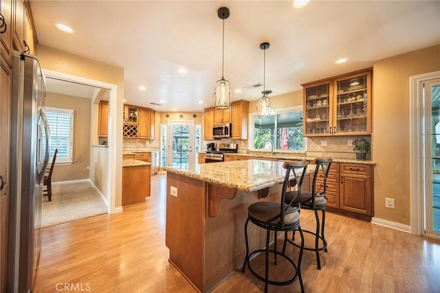 kitchen with decorative light fixtures, a kitchen bar, a center island, light stone counters, and stainless steel appliances