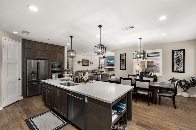 kitchen with wood finished floors, a sink, visible vents, dark brown cabinets, and appliances with stainless steel finishes