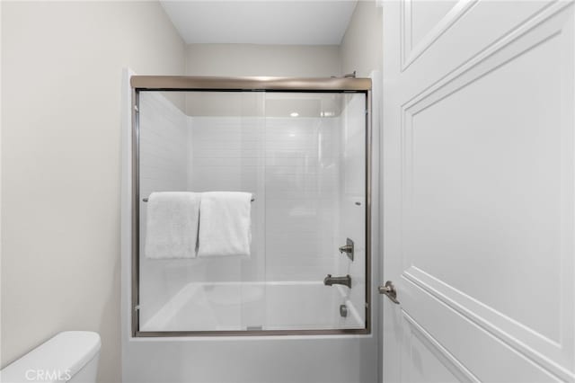 bathroom with toilet and shower / bath combination with glass door