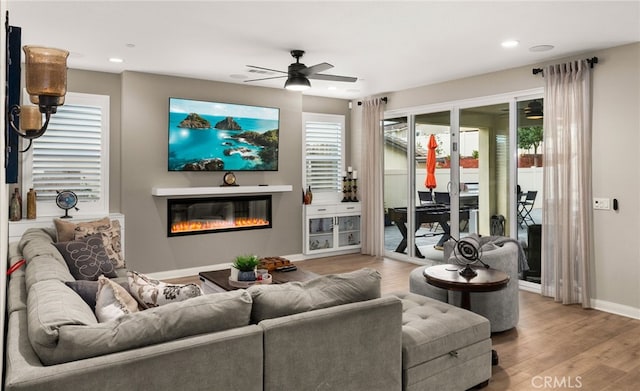 living area with ceiling fan, recessed lighting, wood finished floors, baseboards, and a glass covered fireplace