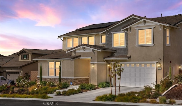 view of front facade featuring driveway, stone siding, an attached garage, roof mounted solar panels, and stucco siding