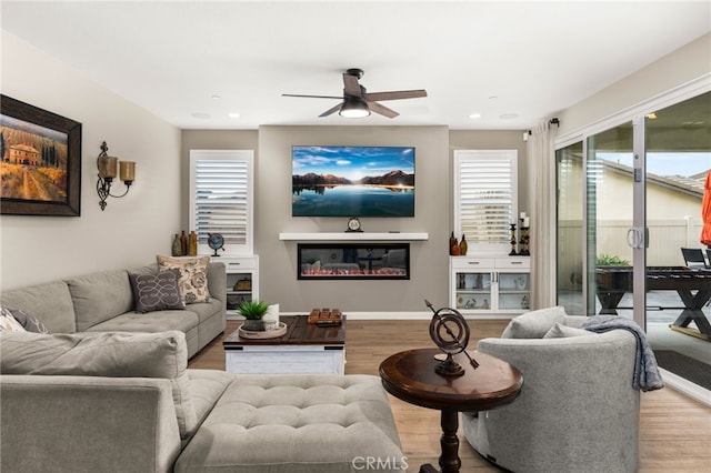 living area with a ceiling fan, a glass covered fireplace, light wood-style flooring, and recessed lighting