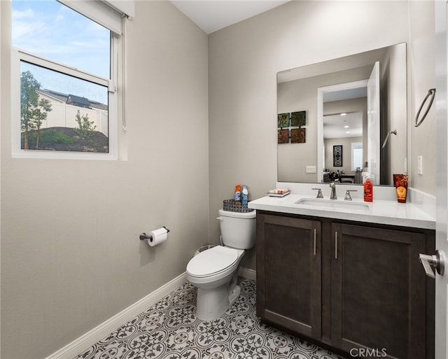 half bathroom with tile patterned flooring, baseboards, vanity, and toilet