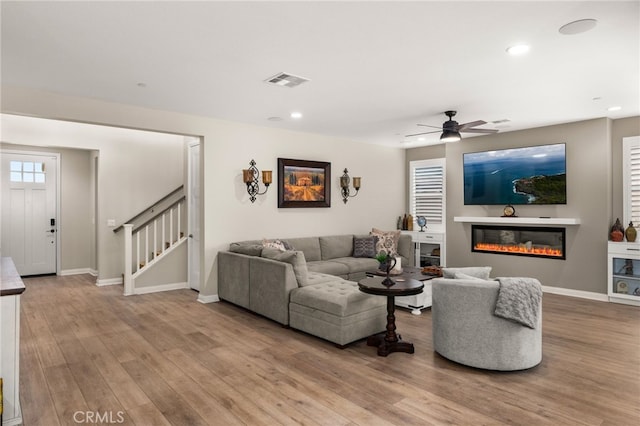 living area featuring light wood-style floors, stairs, visible vents, and a glass covered fireplace