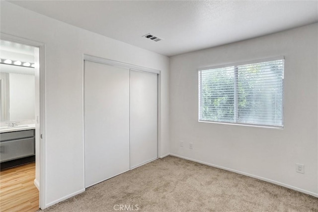 unfurnished bedroom featuring connected bathroom, sink, light carpet, and a closet