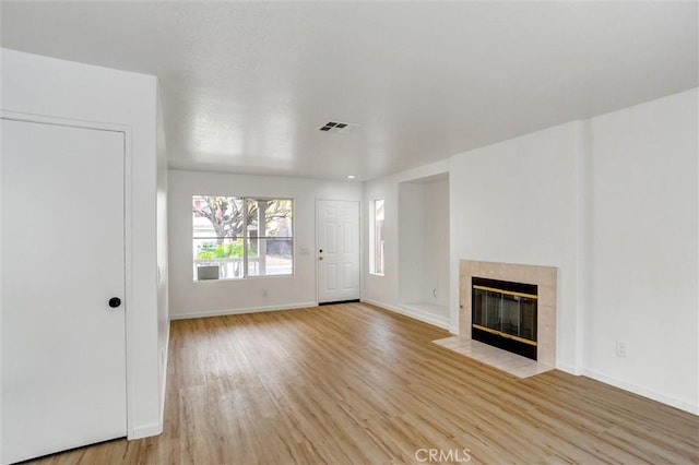 unfurnished living room with a tile fireplace and light wood-type flooring