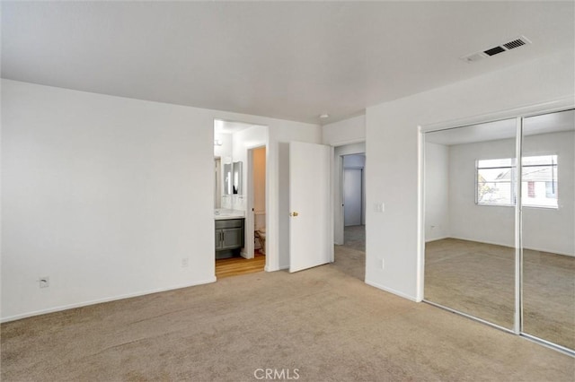 unfurnished bedroom with light colored carpet, ensuite bath, and a closet