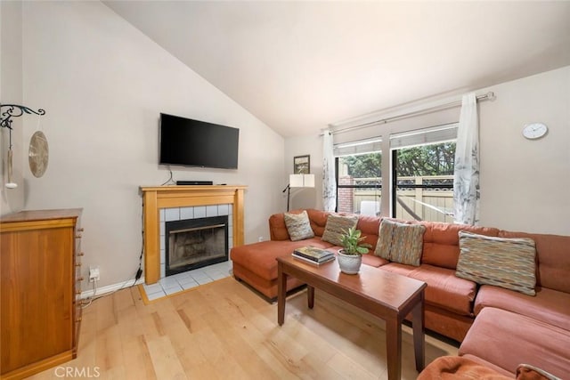 living room featuring a tiled fireplace, high vaulted ceiling, and light hardwood / wood-style floors