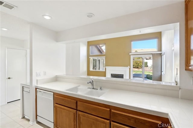 kitchen featuring white dishwasher, sink, and tile counters