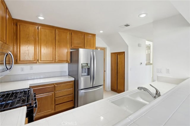 kitchen featuring stainless steel refrigerator with ice dispenser, tile countertops, gas range oven, and sink