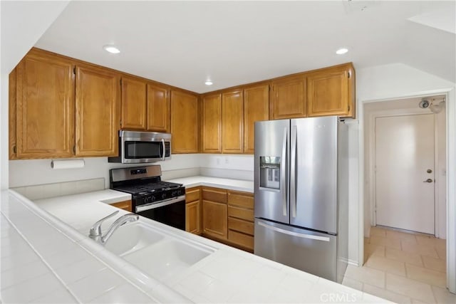 kitchen featuring stainless steel appliances, tile counters, kitchen peninsula, and sink