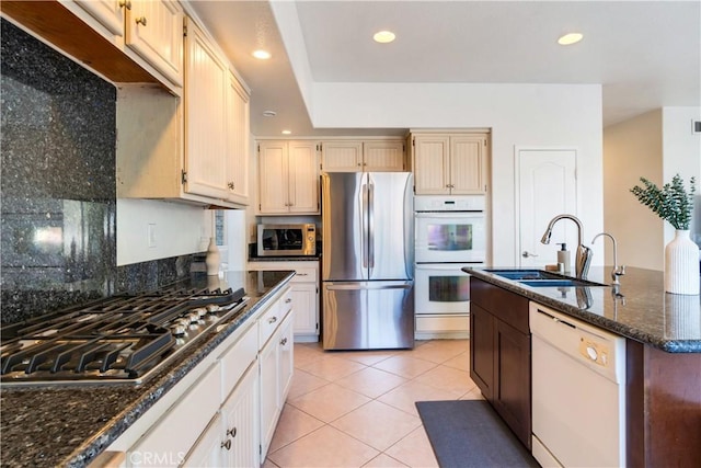 kitchen with light tile patterned floors, stainless steel appliances, sink, and dark stone counters