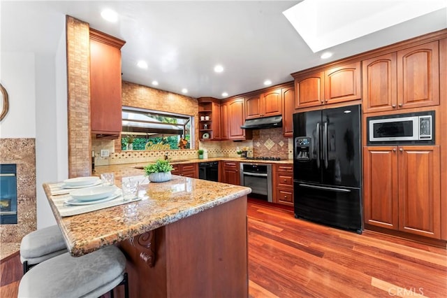 kitchen with a kitchen breakfast bar, light stone counters, black appliances, decorative backsplash, and kitchen peninsula