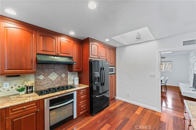 kitchen with appliances with stainless steel finishes, dark wood-type flooring, light stone counters, and decorative backsplash