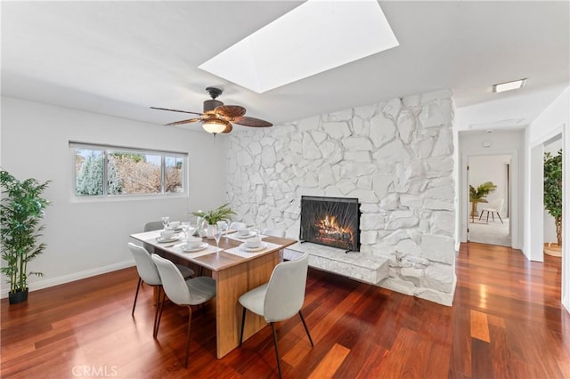 dining room with dark hardwood / wood-style floors, ceiling fan, a fireplace, and a skylight